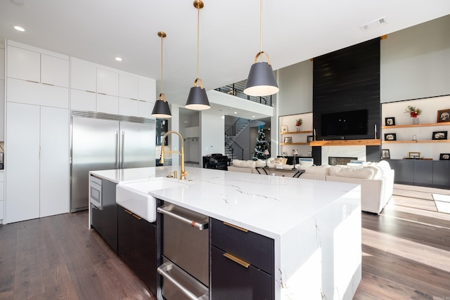 kitchen with sink, dark hardwood / wood-style flooring, stainless steel built in refrigerator, pendant lighting, and a spacious island