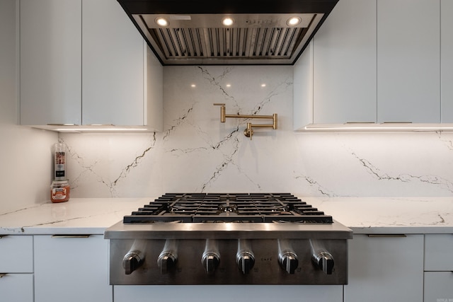 kitchen with stainless steel gas stovetop, white cabinets, wall chimney exhaust hood, light stone countertops, and tasteful backsplash