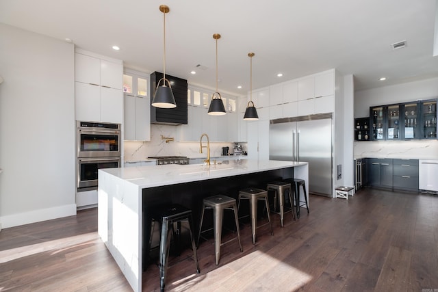 kitchen with white cabinetry, hanging light fixtures, dark wood-type flooring, stainless steel appliances, and a spacious island