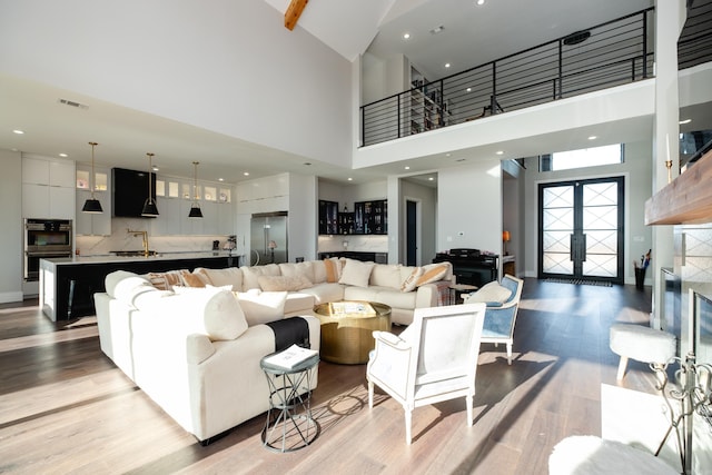 living room with french doors, sink, light hardwood / wood-style floors, and a high ceiling