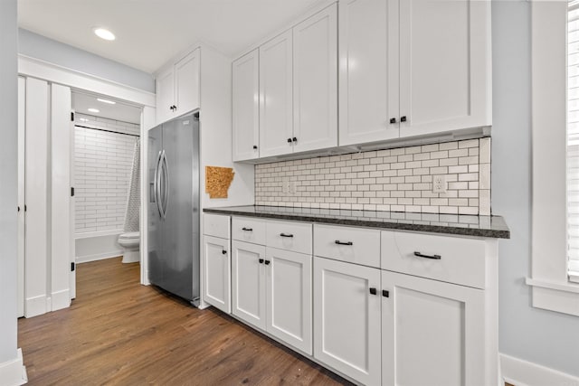 kitchen with backsplash, stainless steel refrigerator with ice dispenser, dark stone countertops, dark hardwood / wood-style flooring, and white cabinetry