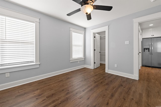 unfurnished bedroom featuring stainless steel refrigerator with ice dispenser, a walk in closet, ceiling fan, dark wood-type flooring, and a closet