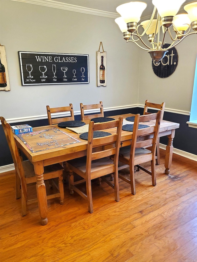 dining space with hardwood / wood-style flooring, ornamental molding, and an inviting chandelier