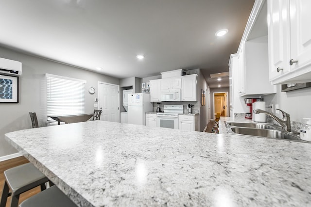 kitchen with white cabinetry, sink, kitchen peninsula, white appliances, and a breakfast bar