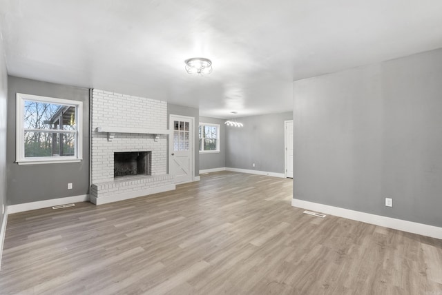 unfurnished living room with light wood-type flooring, a brick fireplace, and a healthy amount of sunlight