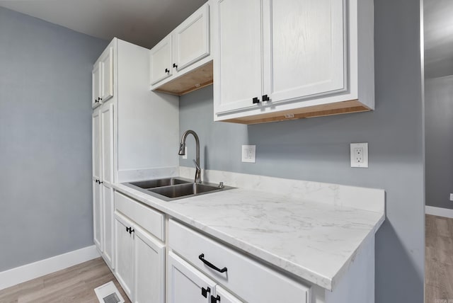 kitchen featuring white cabinets, light wood-type flooring, light stone countertops, and sink