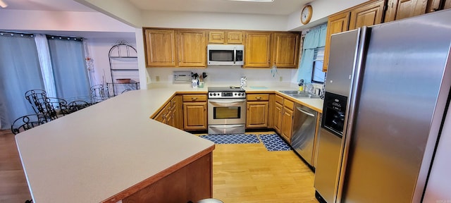 kitchen with light hardwood / wood-style floors, kitchen peninsula, sink, and appliances with stainless steel finishes