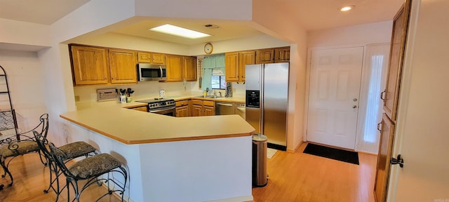 kitchen with sink, light wood-type flooring, appliances with stainless steel finishes, a kitchen bar, and kitchen peninsula