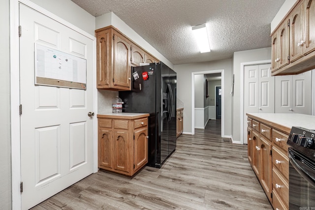 kitchen with black appliances, a textured ceiling, and light hardwood / wood-style flooring