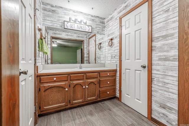 bathroom with wood walls, vanity, wood-type flooring, and a textured ceiling