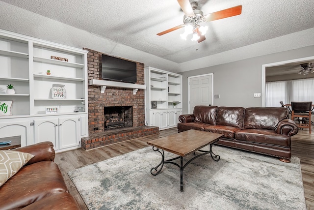 living room featuring a fireplace, light hardwood / wood-style floors, a textured ceiling, and ceiling fan