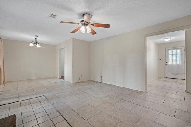 tiled empty room featuring ceiling fan with notable chandelier and a textured ceiling