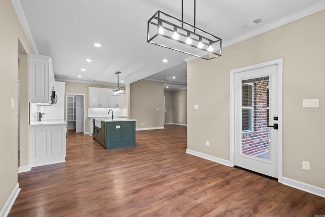 kitchen with white cabinetry, hanging light fixtures, dark hardwood / wood-style floors, crown molding, and a kitchen island with sink