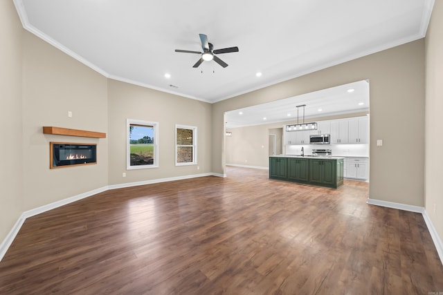 unfurnished living room featuring crown molding, ceiling fan, and dark wood-type flooring