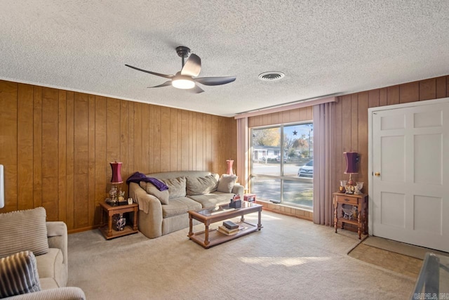 living room featuring wood walls, ceiling fan, light colored carpet, and a textured ceiling