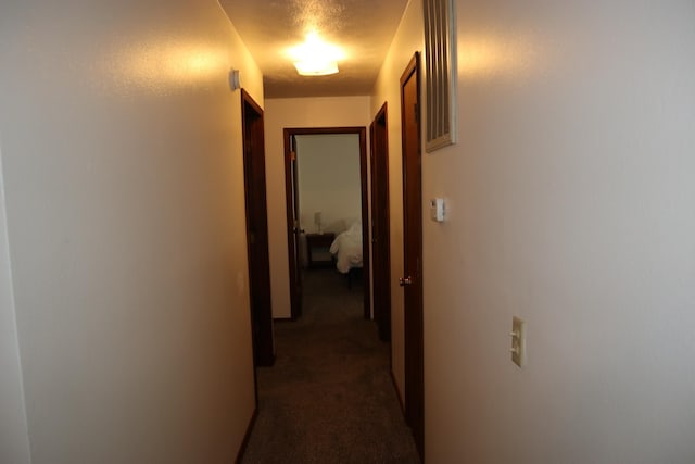 hall with a textured ceiling and dark colored carpet