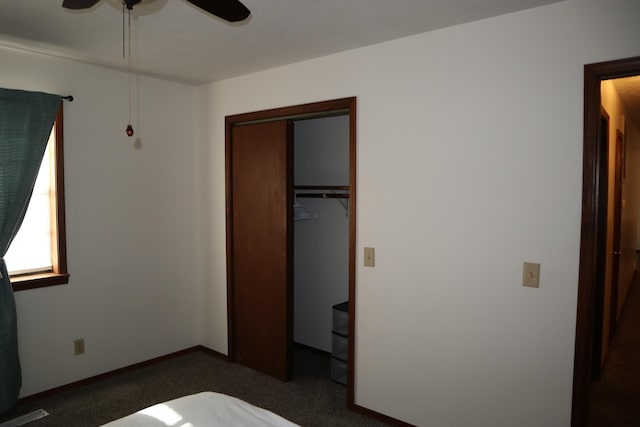 unfurnished bedroom with ceiling fan, dark carpet, and a closet