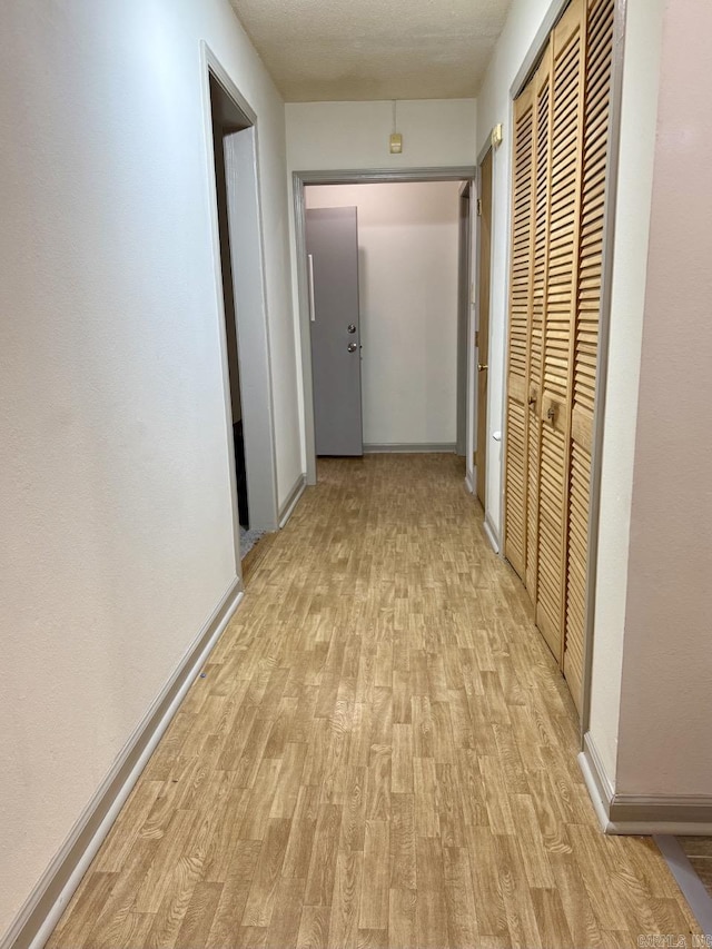 hallway with light hardwood / wood-style floors and a textured ceiling