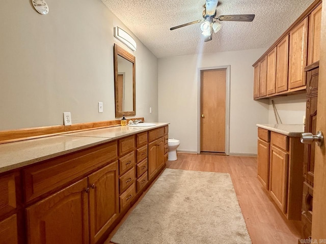 bathroom with vanity, a textured ceiling, ceiling fan, hardwood / wood-style floors, and toilet