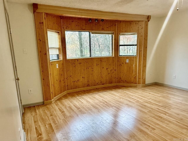 empty room featuring a textured ceiling, light wood-type flooring, and wooden walls