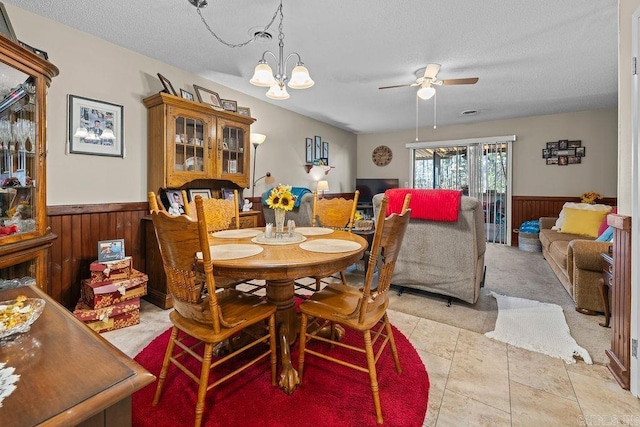 carpeted dining space with a textured ceiling, ceiling fan with notable chandelier, and wooden walls