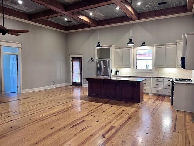 kitchen with a center island with sink, white cabinets, light hardwood / wood-style flooring, beamed ceiling, and decorative light fixtures