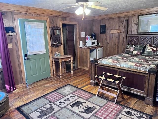 bedroom featuring a textured ceiling, wooden walls, ceiling fan, and dark wood-type flooring