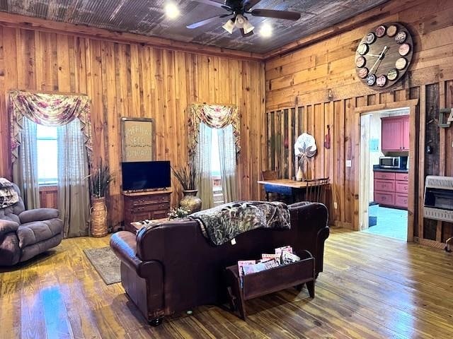 living room featuring wood-type flooring, heating unit, ceiling fan, and wooden walls