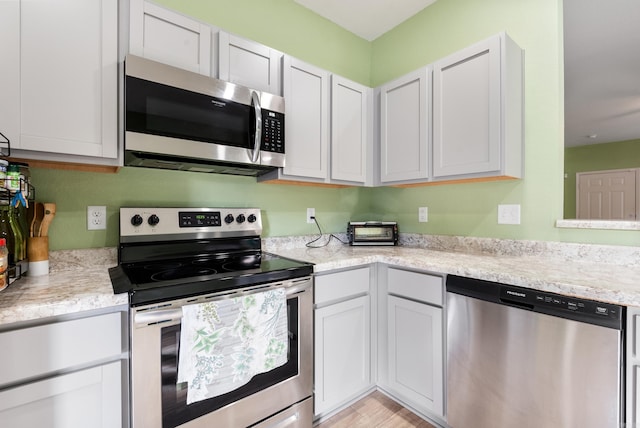 kitchen featuring light stone counters, white cabinets, stainless steel appliances, and light wood-type flooring