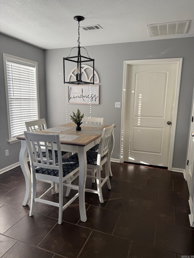 dining room with a notable chandelier, dark tile patterned floors, and a textured ceiling