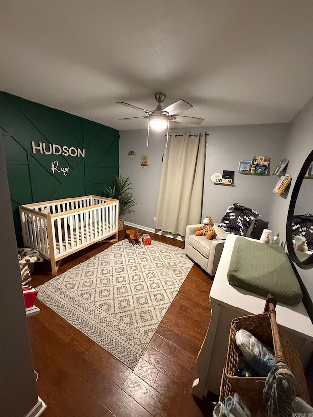 bedroom with ceiling fan, dark wood-type flooring, and a crib