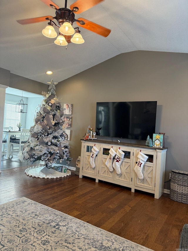 living room featuring ceiling fan with notable chandelier, dark hardwood / wood-style flooring, and vaulted ceiling