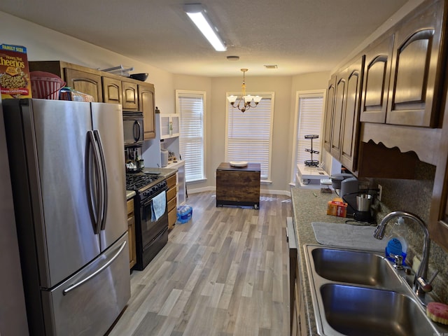 kitchen with an inviting chandelier, black appliances, sink, hanging light fixtures, and light hardwood / wood-style flooring