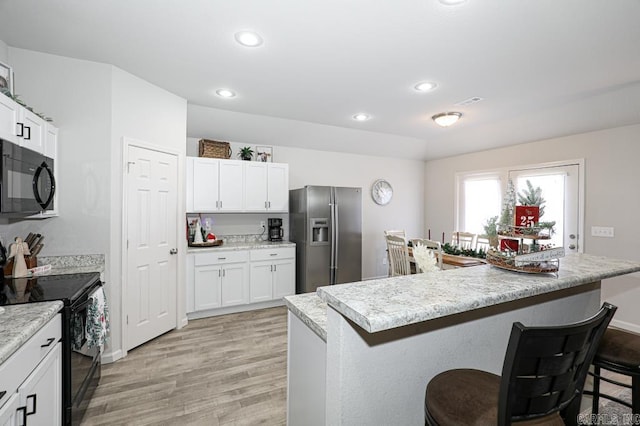 kitchen featuring a center island, light hardwood / wood-style floors, a kitchen bar, white cabinets, and black appliances