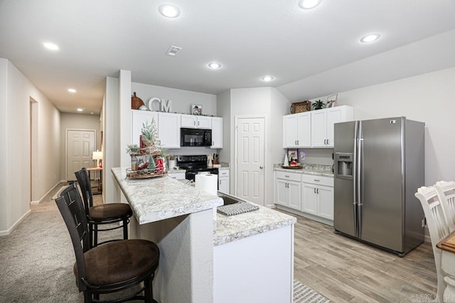 kitchen with a kitchen bar, kitchen peninsula, black appliances, light hardwood / wood-style floors, and white cabinetry