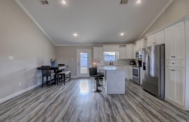 kitchen featuring appliances with stainless steel finishes, ornamental molding, light hardwood / wood-style flooring, white cabinets, and a center island