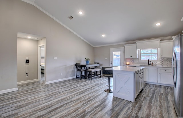 kitchen featuring stainless steel fridge, light wood-type flooring, ornamental molding, white cabinets, and a center island