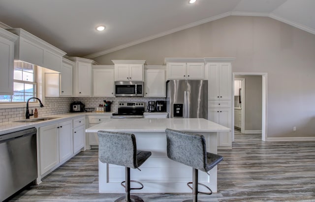 kitchen with crown molding, sink, vaulted ceiling, appliances with stainless steel finishes, and a kitchen island