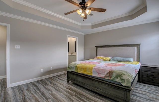 bedroom with a raised ceiling, connected bathroom, and ornamental molding