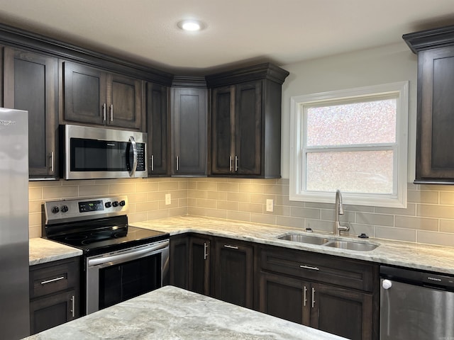 kitchen featuring decorative backsplash, appliances with stainless steel finishes, light stone countertops, dark brown cabinets, and sink