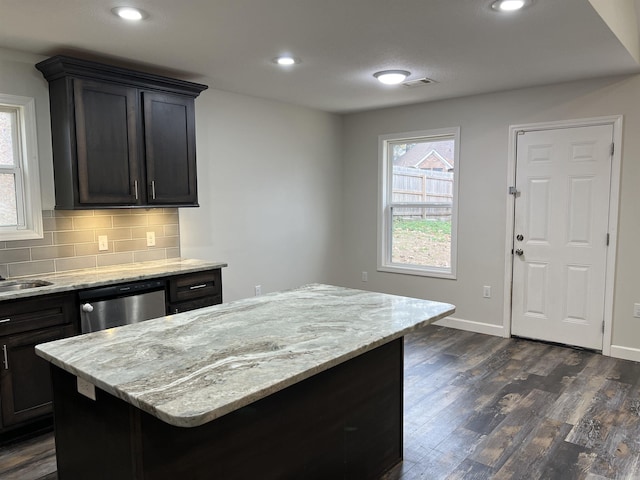 kitchen with dishwasher, a center island, backsplash, dark wood-type flooring, and light stone countertops