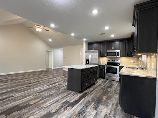 kitchen with sink, dark hardwood / wood-style floors, vaulted ceiling, a kitchen island, and appliances with stainless steel finishes