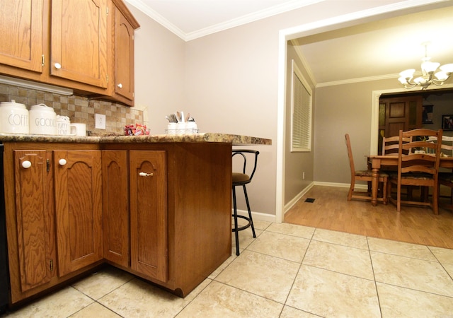 kitchen featuring backsplash, ornamental molding, an inviting chandelier, stone counters, and light tile patterned flooring