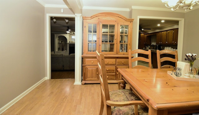 dining space with decorative columns, crown molding, ceiling fan with notable chandelier, and light wood-type flooring