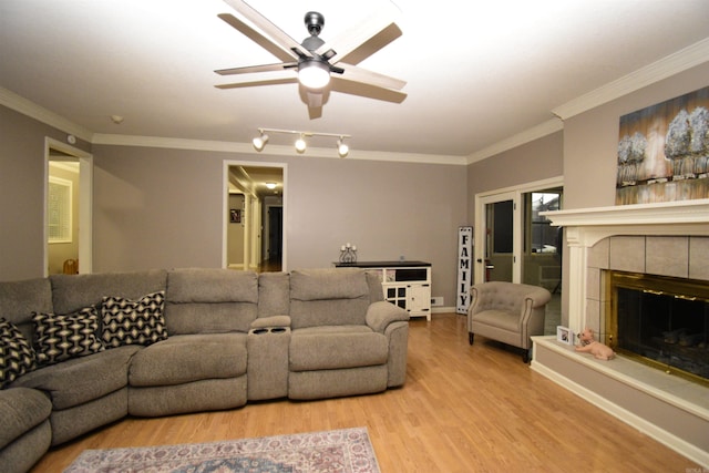 living room featuring light wood-type flooring, ceiling fan, ornamental molding, and a tiled fireplace