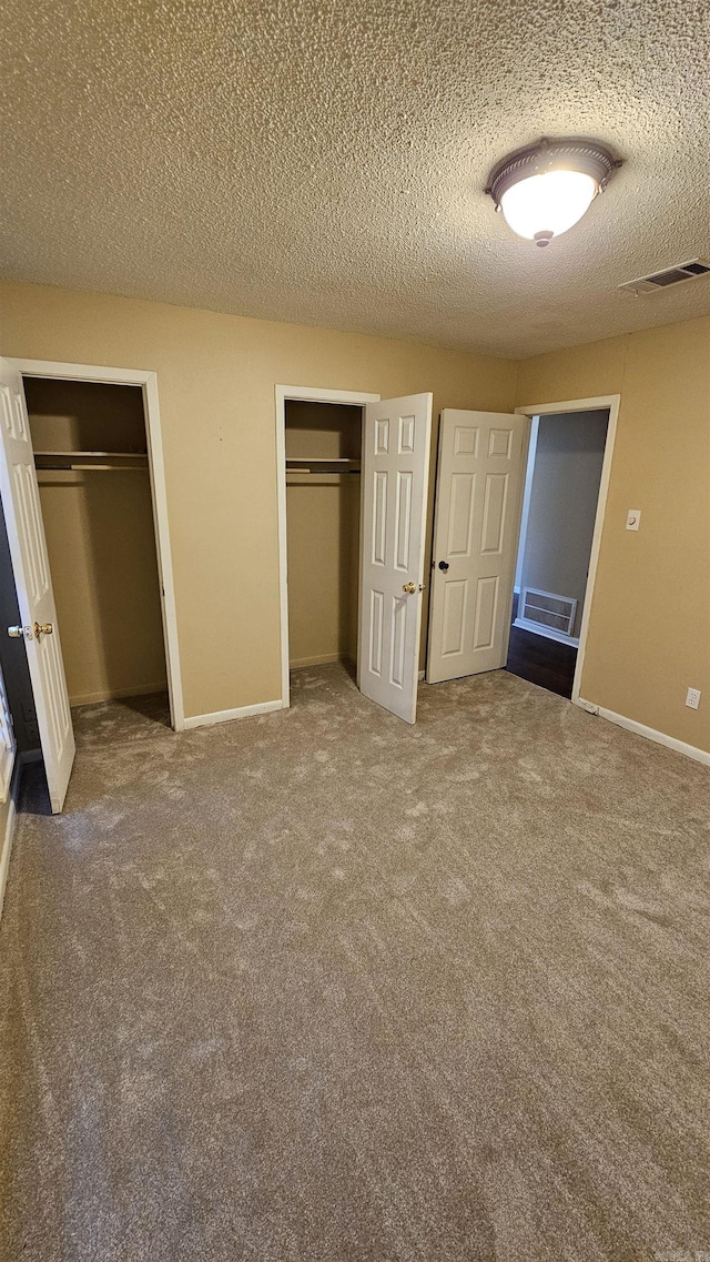 unfurnished bedroom featuring carpet floors, a textured ceiling, and two closets