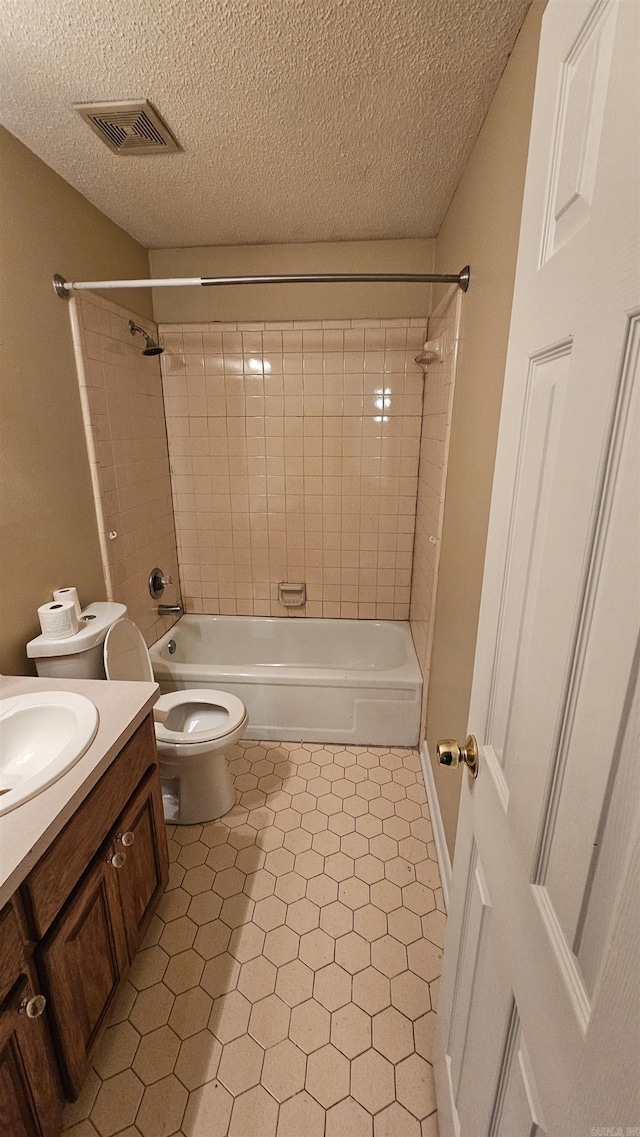 full bathroom featuring tiled shower / bath combo, tile patterned floors, a textured ceiling, toilet, and vanity