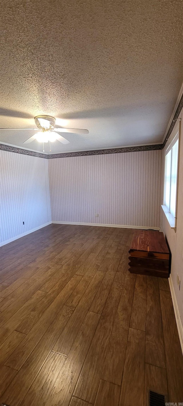 empty room with ceiling fan, wood walls, dark hardwood / wood-style flooring, and a textured ceiling