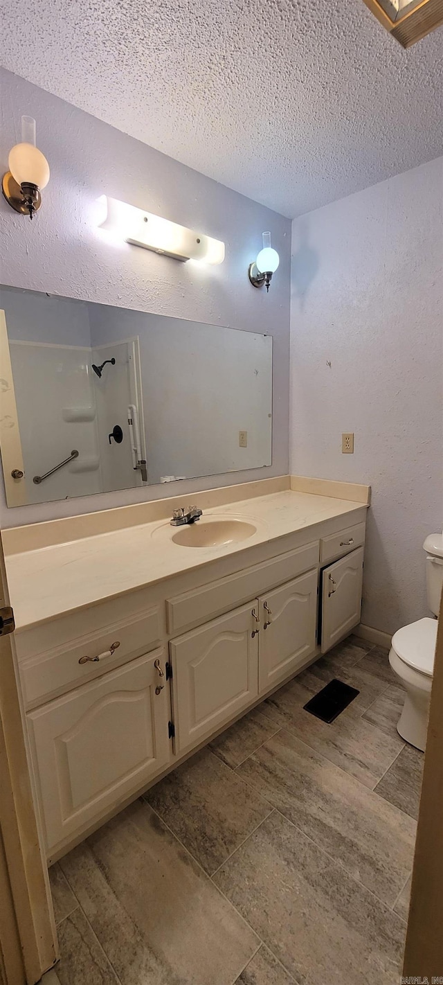 bathroom featuring vanity, a textured ceiling, a shower, hardwood / wood-style flooring, and toilet