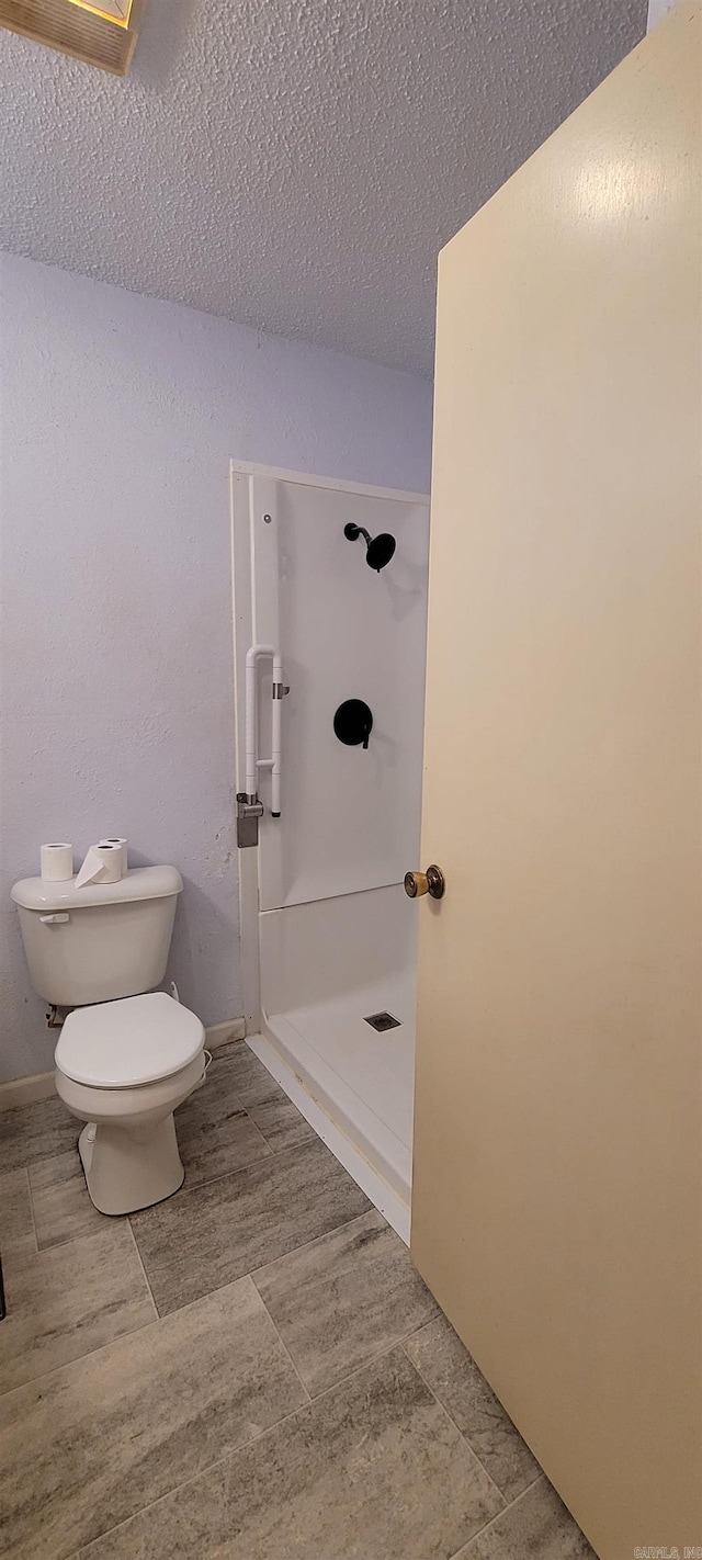 bathroom with a textured ceiling, toilet, and walk in shower